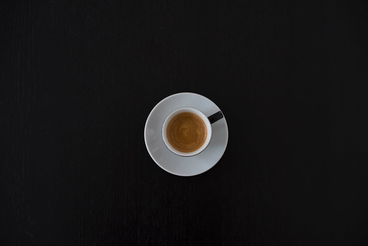 Flat lay of a white coffee cup with espresso on a black table, highlighting minimalist design.